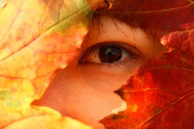 Detalle de una mujer ocultándose bajo hojas de otoño