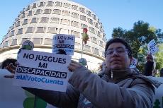 Persona con discapacidad ante el Constitucional con un cartel que dice: "No juzgues mi discapacidad"