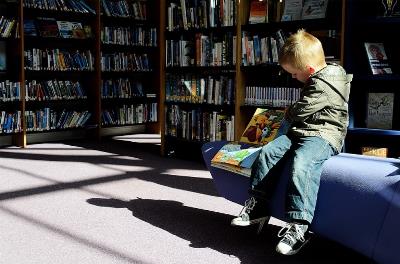 Un niño leyendo y sentado en la biblioteca de un colegio