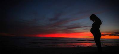 Perfil de una mujer embarazada en una playa, durante la puesta de sol o antes del amanecer