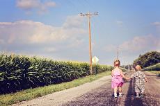 Dos niños de la mano se alejan por un camino rural