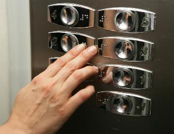 Una persona busca una planta dentro de un ascensor usando braille.