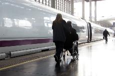 Una persona en silla de ruedas se dirige a un tren, acompañada por una ayudante