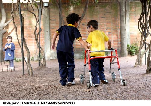 Imagen de un niño con discapacidad en un recreo, junto a otro niño sin discapacidad aparente