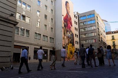 Un grupo de personas caminan por la calle, acercándose a contemplar el mural de Case Maclaim, The Fabulous Tale Of Being Different