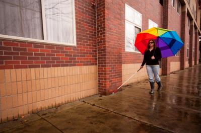 Persona ciega andando bajo la lluvia junto a un edificio