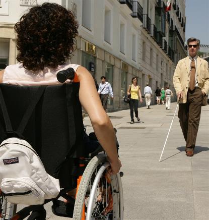 Un hombre ciego y una mujer en silla de ruedas en una calle de una ciudad 