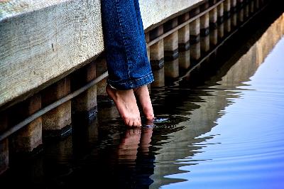 Detalle de las piernas de una mujer en vaqueros metiendo los dedos de los pies en el agua