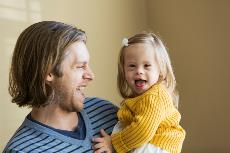 Padre sonriendo con su hija con síndrome de Down en sus brazos